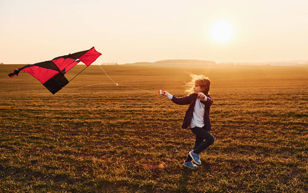 Happy little girl running with kite in hands on the beautiful field at sunrishe time. - Foto, afbeelding