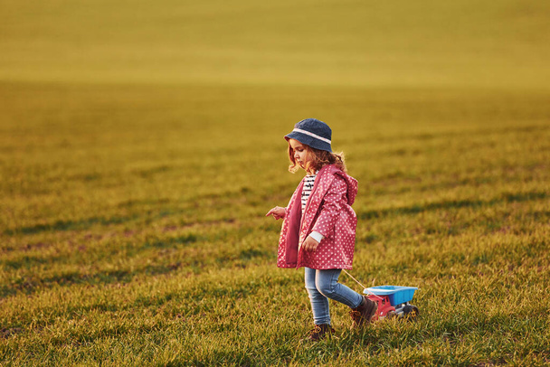 Cute little girl walks with toy car on the beautiful field at sunny daytime. - Fotó, kép
