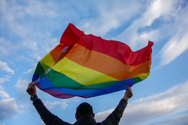 Man holding a Gay Rainbow Flag over blue summer sky. Bisexual, gay, lesbian, transsexual symbol. - Foto, Imagen