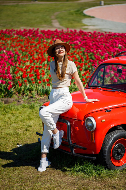 Portrait of young pretty woman leaning over rustic cabriolet car in colorful tulip fields. Chilliwack Tulip Ftstival. British Columbia. Canada - Fotó, kép