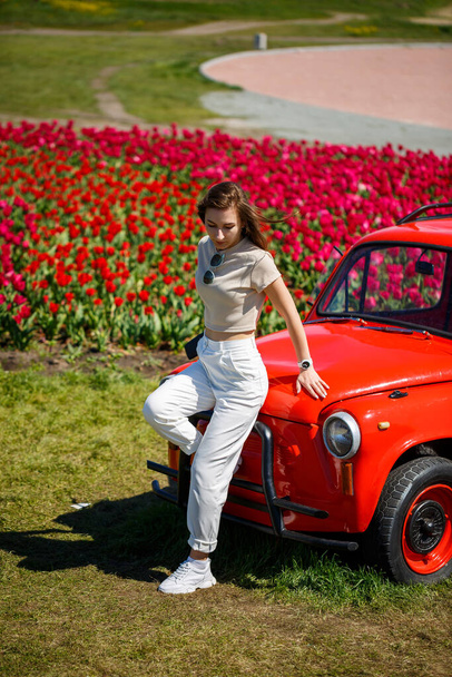 Portrait of young pretty woman leaning over rustic cabriolet car in colorful tulip fields. Chilliwack Tulip Ftstival. British Columbia. Canada - 写真・画像