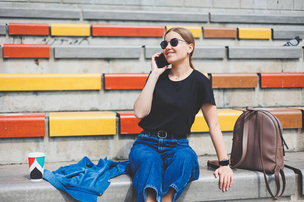Jovem mulher de negócios elegante sentado nos passos e segurando um telefone e uma xícara de café - Foto, Imagem