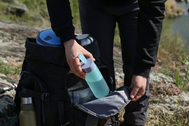 Hiker putting bottle of water into backpack outdoors, closeup - Foto, Imagen