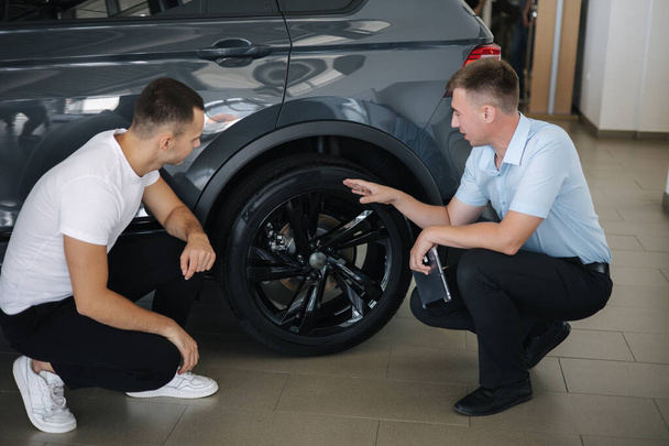 Salesperson selling cars at car dealership. Man choosing car in car showroom. Show the size of the discs and tires - Foto, imagen