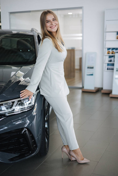Portrait of gorgeous woman in showroom. Beautiful salesperson standing by car. Blond hair female after seles car - 写真・画像
