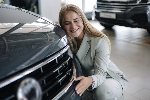 Business woman chossing a new car in a car showroom. Happy female hug new car and very glad. Elegant female in suit - Photo, Image