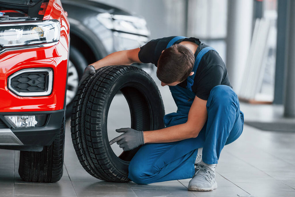 Man in uniform changing tire of automobile. Conception of car service. - Foto, imagen