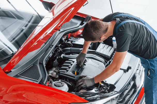Top view of male worker in uniform that repairs red automobile. - 写真・画像