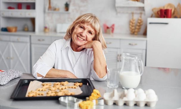 Senior woman cooks Christmas cookies on the kitchen at daytime. - Foto, afbeelding
