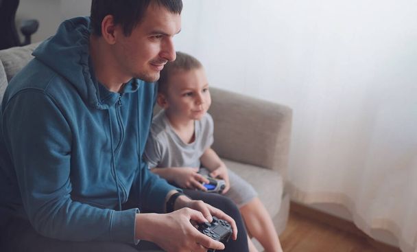 Happy father and son sit in the living room on the sofa and play or watch TV - 写真・画像