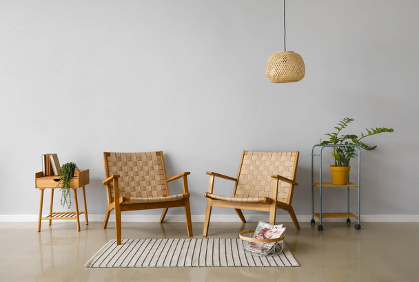 Modern armchairs, table, houseplant and lamp near light wall - 写真・画像