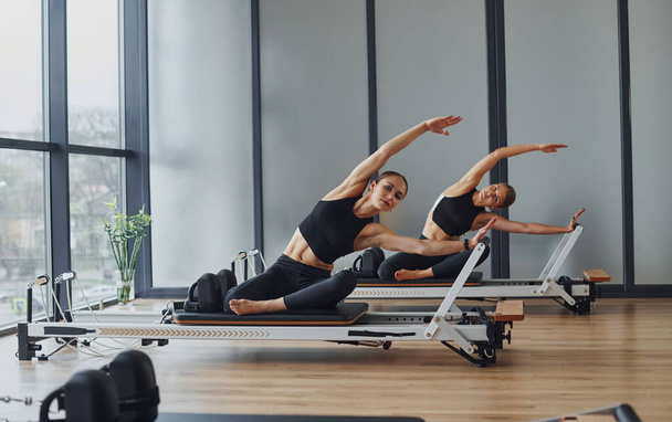 Using gym equipment. Two women in sportive wear and with slim bodies have fitness yoga day indoors together. - Фото, изображение