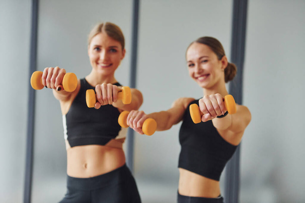 Uses dumbbells. Two women in sportive wear and with slim bodies have fitness yoga day indoors together. - Photo, Image