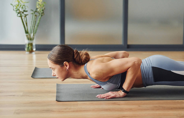 Doing push ups. Young woman in sportive wear and with slim body have fitness yoga day indoors. - Foto, afbeelding