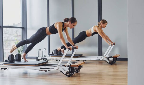 Using gym equipment. Two women in sportive wear and with slim bodies have fitness yoga day indoors together. - Fotoğraf, Görsel