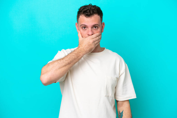 Mladý brazilský muž izolované na modrém pozadí pokrytí úst s rukou - Fotografie, Obrázek