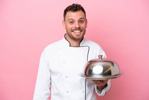 Молодой бразильский шеф-повар с подносом на розовом фоне с неожиданным выражением лица - Фото, изображение