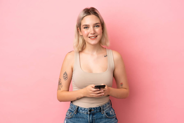 ピンクの背景に孤立した若い白人女性が携帯電話でメッセージを送る - 写真・画像