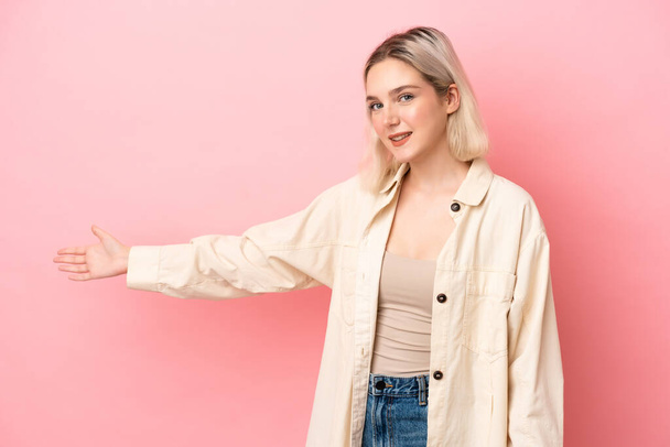Young caucasian woman isolated on pink background extending hands to the side for inviting to come - Photo, Image