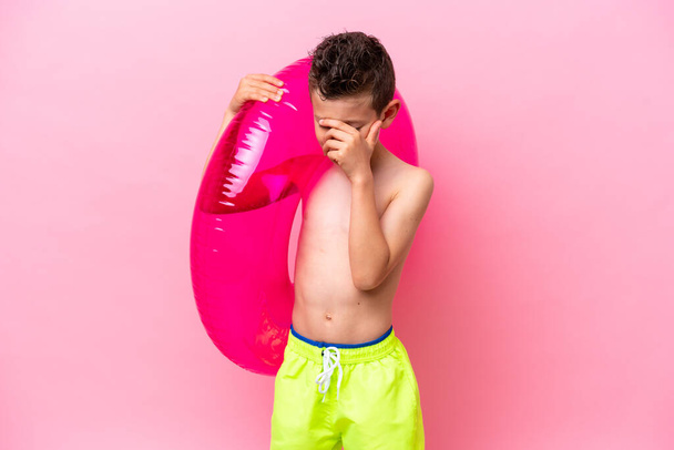 Little caucasian boy holding a inflatable donut isolated on pink background laughing - Valokuva, kuva