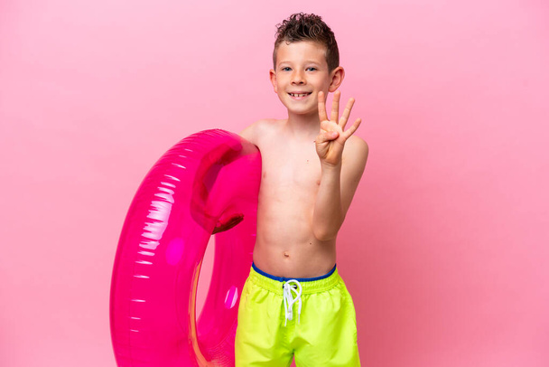 Petit garçon caucasien tenant un beignet gonflable isolé sur fond rose heureux et comptant quatre avec les doigts - Photo, image