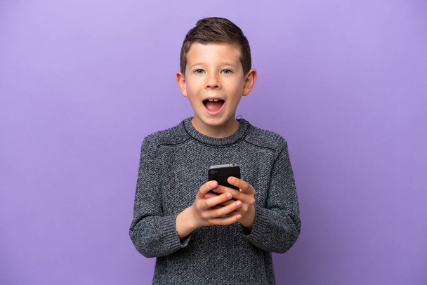 Маленький мальчик, изолированный на фиолетовом фоне, удивлен и посылает сообщение - Фото, изображение