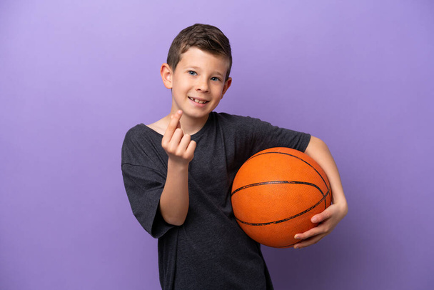 紫色の背景に孤立したバスケットボールをしている小さな男の子お金のジェスチャーを作る - 写真・画像