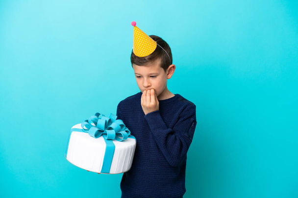 Μικρό αγόρι που κρατάει τούρτα γενεθλίων απομονωμένο σε μπλε φόντο έχοντας αμφιβολίες - Φωτογραφία, εικόνα