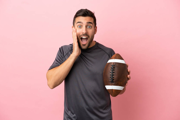 Young caucasian man playing rugby isolated on pink background with surprise and shocked facial expression - Фото, изображение