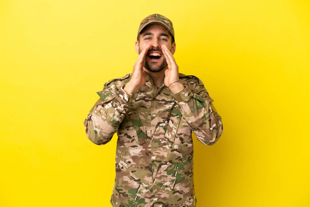 Wojskowy odizolowany na żółtym tle krzyczy i coś ogłasza - Zdjęcie, obraz
