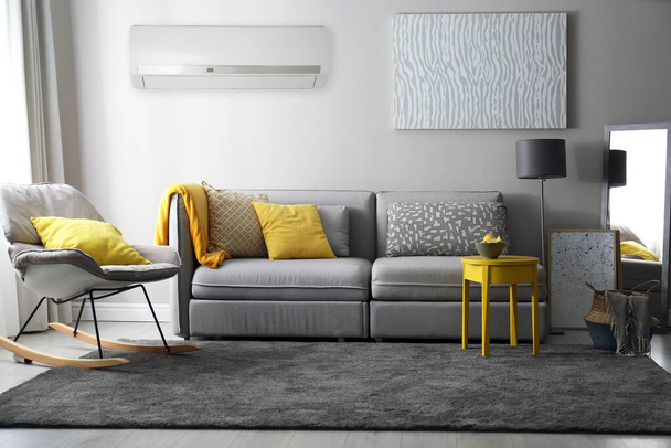 Modern air conditioner on light grey wall in living room with stylish furniture - Fotó, kép