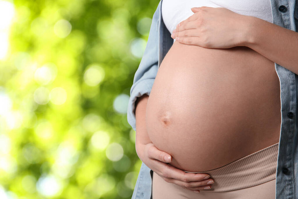 Mladá těhotná žena se dotýká svého břicha venku, detailní záběr. Mezera pro text - Fotografie, Obrázek