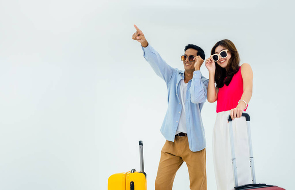 Ready to travel, happy holiday. Summer vacation. Asian couple in sunglasses with pointing and looking forward with exciting, young woman and man with suitcase on trip, isolated on white background. - Fotografie, Obrázek
