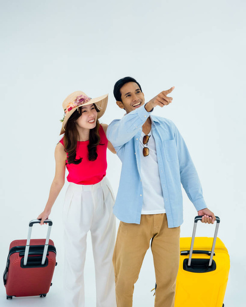 Exciting travel, happy holiday. Summer vacation. Asian couple travelers looking out with exciting, young man and woman pointing and walking with suitcases, isolated on white background, vertical. - Foto, imagen