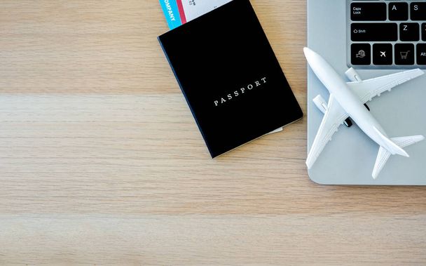 Reisepass schwarzer Einband mit Flugticket in der Nähe des Laptops und weißes Flugzeugspielzeug auf Holzschreibtisch mit Kopierraum, Draufsicht. Online-Ticketbuchung für Reisekonzept. - Foto, Bild