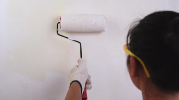 Jonge vrouw decorateur draagt beschermende bril verft de muren met een roller. Reparatie en interieur. - Video