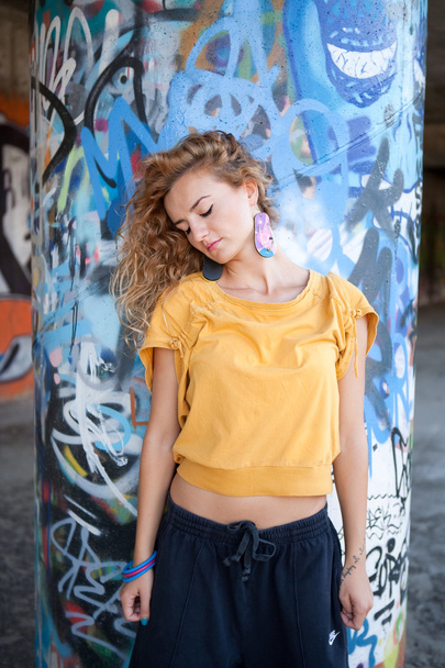 Beautiful hip teenage blonde woman standing by graffiti wall - Φωτογραφία, εικόνα