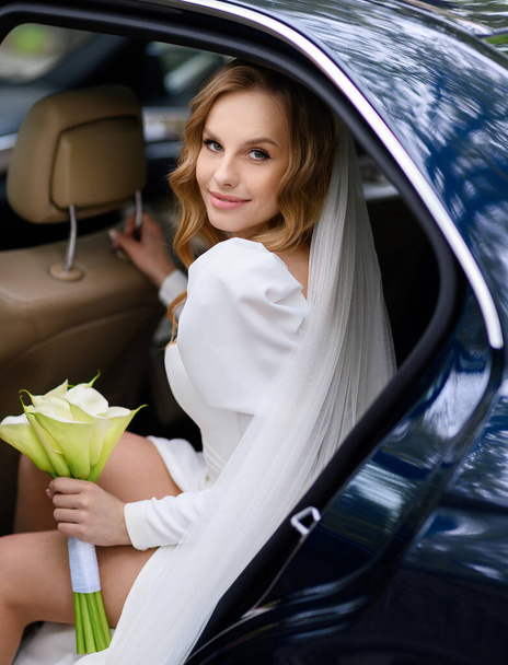 Schöne kaukasische blonde Braut sitzt in einem stilvollen Auto mit einem Strauß - Foto, Bild