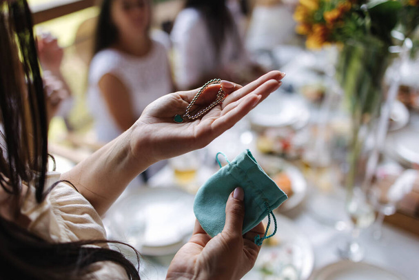 Подарок для именинницы браслета с подвеской в форме сердечно-бирюзового цвета. Женщины держатся за руки. День рождения на открытом воздухе - Фото, изображение