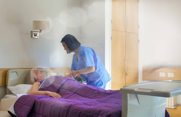 Ασιάτισσα γιατρός που βοηθάει ηλικιωμένη γυναίκα στο κρεβάτι του νοσοκομείου. Αποκατάσταση και συνταξιοδότηση. - Φωτογραφία, εικόνα