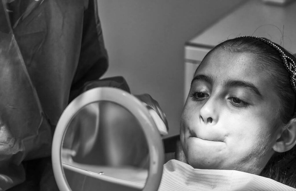 Giovane femmina caucasica sorridente mentre dentista in guanti di lattice bianco controllare le condizioni dei suoi denti. bambina in sedia dentale blu. - Foto, immagini
