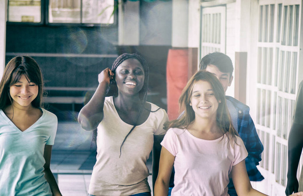 Szczęśliwa, wieloetniczna grupa nastolatków w szkole spacerująca korytarzem. Koncepcja szczęśliwości i lekkości. - Zdjęcie, obraz