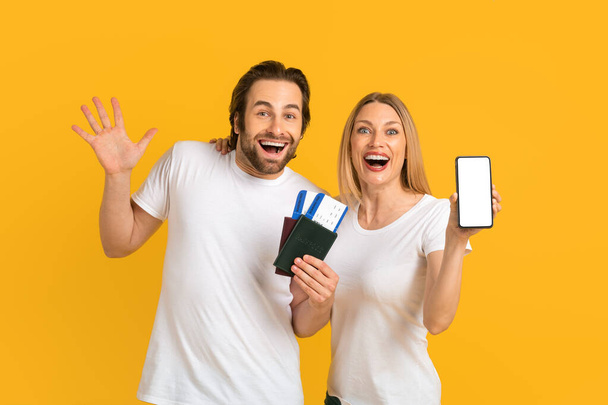 Задоволена молода єврозова пара показує смартфон з порожнім екраном і паспортами з квитками на повітря. - Фото, зображення