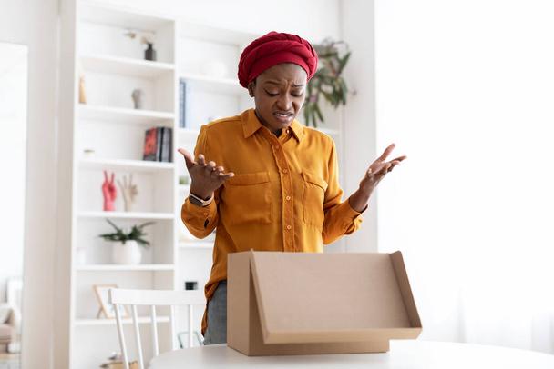 Disappointed african american woman looking inside delivery box at home - Foto, afbeelding