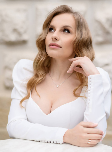 Beautiful bride sitting on a chair and posing on the background of the castle - Zdjęcie, obraz