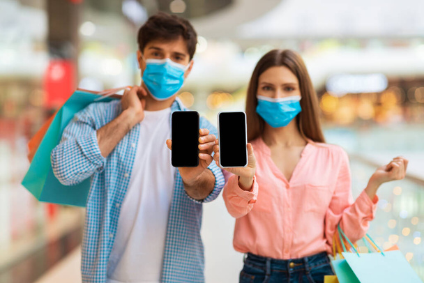 Couple On Shopping Showing Smartphones Wearing Masks In Modern Mall - Foto, afbeelding