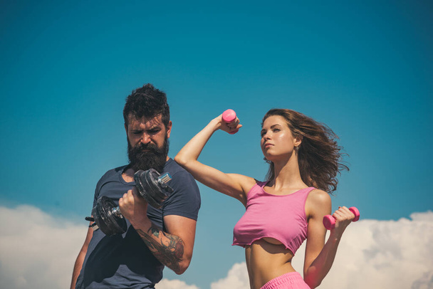 Sporty couple with dumbbell outdoors. Couple working out with dumbbells. Fitness club outside on nature. Fitness sexy models pumping up arm with dumbbell. - Photo, image