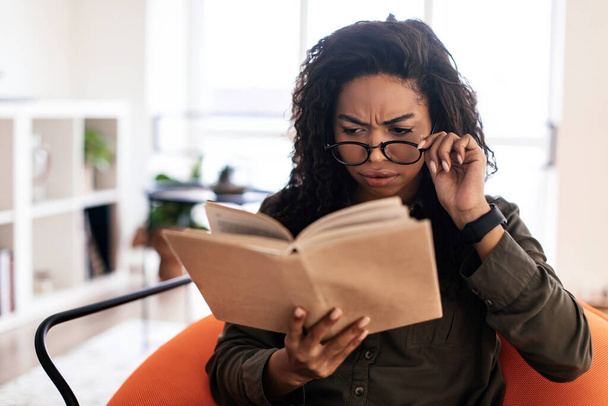 Összezavarodott fekete hölgy szemüvegben, aki könyvet próbál olvasni. - Fotó, kép