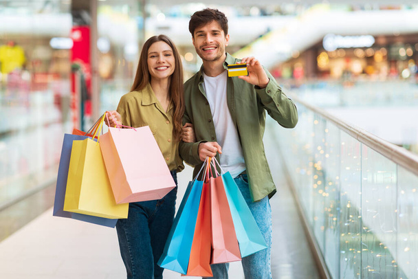 Веселая пара показывает покупки кредитных карт в современном гипермаркете - Фото, изображение