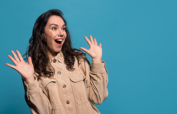 Happy surprised excited young european brunette woman in casual with raised hands looking to empty space - 写真・画像